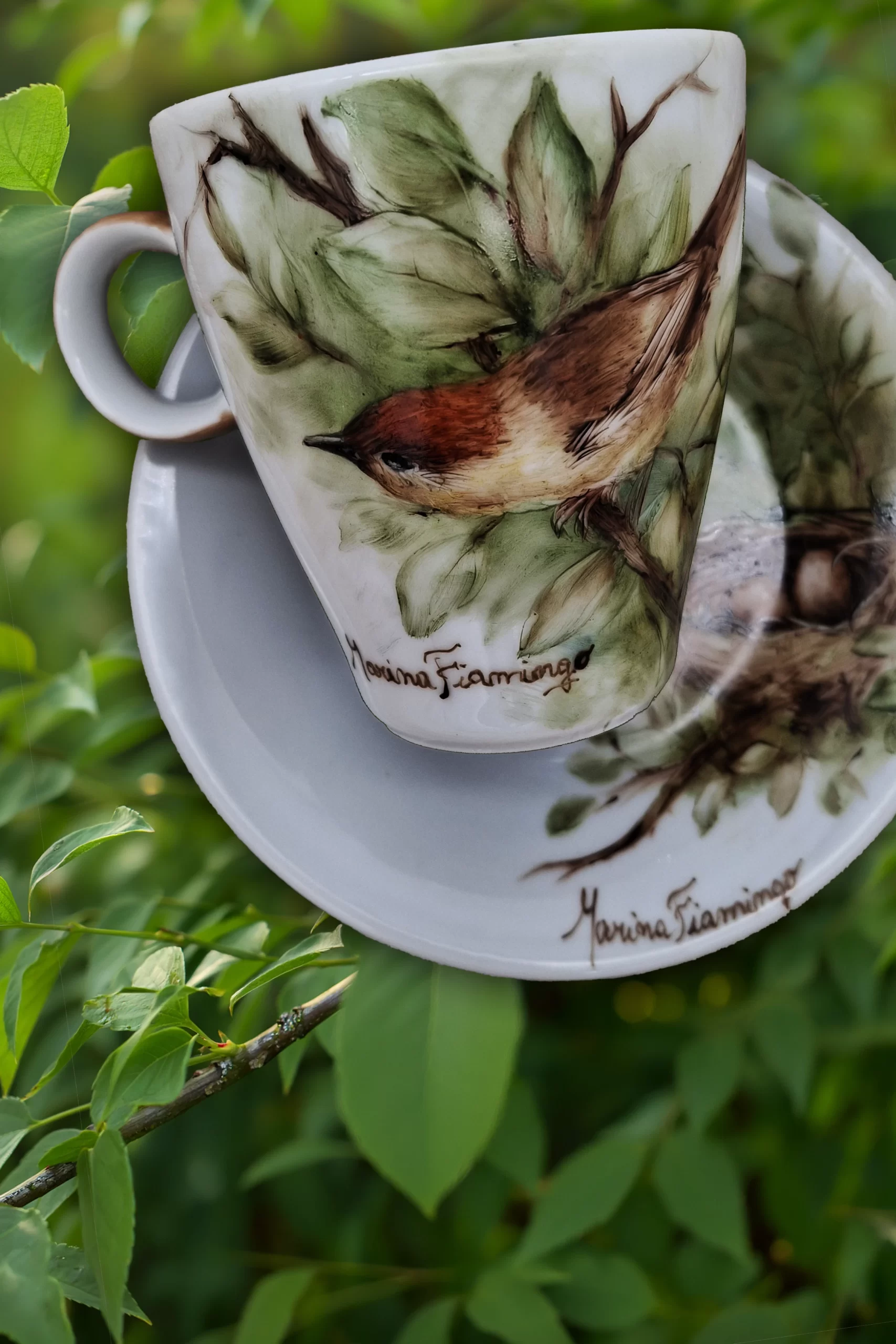 Hand-painted porcelain cup featuring a small bird among green leaves, demonstrating Marina Fiamingo's inspiration from nature.